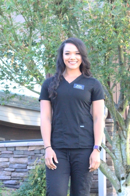 Destinee wearing dark scrubs against a nature background.