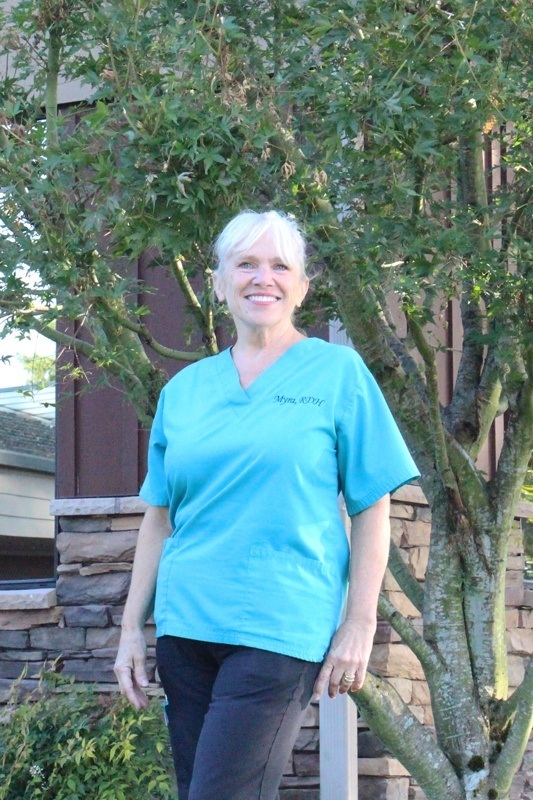 Myra wearing an aqua scrub shirt against a nature and building background.