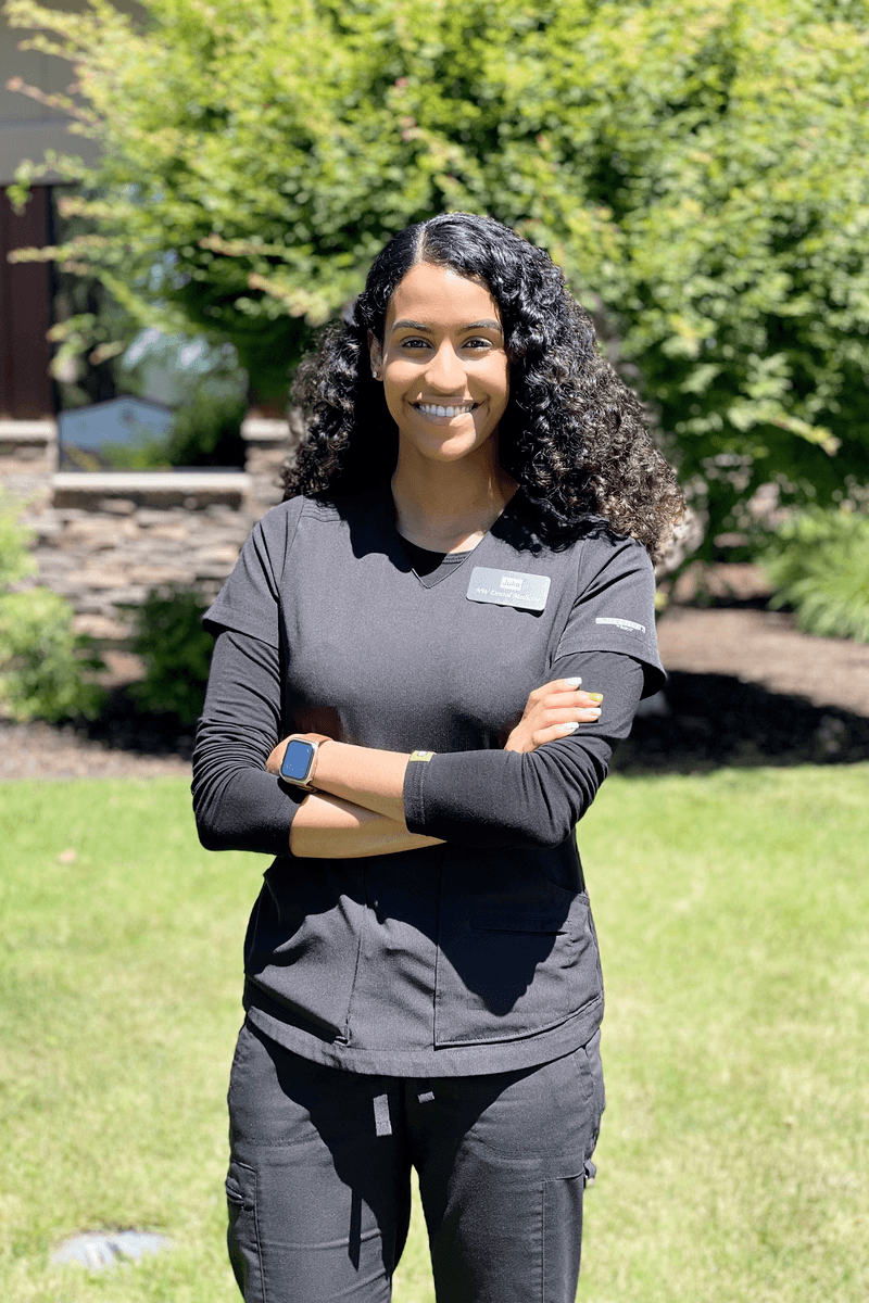 Destinee wearing dark scrubs against a nature background.